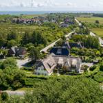 Haus mit Dachrinne, umgeben von Grünflächen und Straße. Blick auf Meer und Dorf.