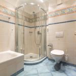 Badezimmer mit Dusche, Badewanne und Toilette. Fliesen mit floraler Bordüre.