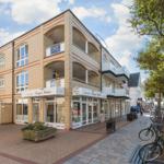 Gebäude mit Laden und Balkonen an einer Straße mit Bäumen und Fahrrädern.