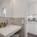 Sink with mirror and three green bottles. Kitchen with white cabinets and coffee machine.