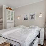 Bedroom with double bed, cabinet, and kitchen area. Wall art and lamps provide lighting.
