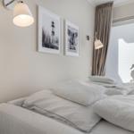 Bedroom with white bed, wall pictures, and window with blinds.