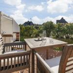 Deck with wooden table, chairs, and sunshade. View of greenery and buildings.