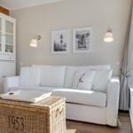 White sofa with cushions, wicker chest, and pictures on the wall.