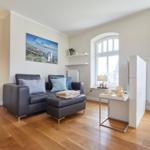 Wohnzimmer mit Sofa, Holzboden und großen Fenstern.
