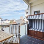 Terrasse mit Liege, Tisch und Stühlen. Blick auf Wohnhäuser und Himmel.