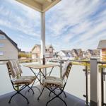 Terrasse mit Tisch und zwei Stühlen, Blick auf Wohnhäuser und Straße.
