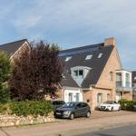 Modernes Haus mit Solaranlage und Balkonen. Zwei Autos parken vor dem Eingang.