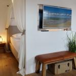 Schlafzimmer mit Bett, Fernseher und Pflanze.
