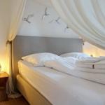 Himmelbett mit weißen Laken, Vorhängen und Vogeldekoration an der Wand.