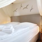 Doppelbett mit weißer Bettwäsche und Handtüchern. Wanddekoration mit Vögeln. Nachttisch mit Laterne.