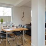 Esszimmer mit Holztisch, Stühlen und Fenster. Wohnzimmer mit Sofa und Wandbild.