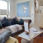 Wohnzimmer mit Sofa, Kissen und Glas-Tisch. Wandbild mit Seemöwe. Holzboden und weißer Schrank.