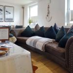 Lounge mit braunem Sofa, Kissen und Tisch. Wanddekoration mit Anker und Bildern.