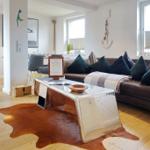 Wohnzimmer mit braunem Sofa, Metalltisch und Lederhaut auf Holzboden.