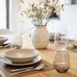 Dining table with dishes, glasses, and vase flowers.