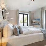 Bedroom with bed, windows, and wall art. Wall with fish motif and standing lamp.