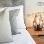 Bedroom with bed, pillows, and nightstand with lamp. Wall with fish motifs.