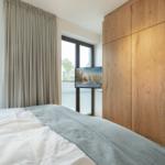 Bedroom with bed, wooden wardrobe, and TV. Windows with blinds and curtains.