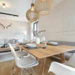 Dining area with wooden table and white chairs, next to living area with sofa and deer head on wall.