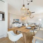 Dining room with wooden table, white chairs, and modern pendant lights. Kitchen area with built-in oven.