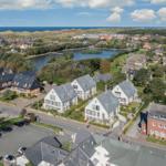 Aerial view of a coastal village with houses, a lake, and the sea in the background.