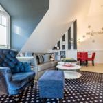 Living area with blue upholstered chair, sofa, and star-patterned rug under sloped ceiling.