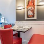 Dining table with red chairs and wall art on gray wall.