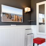 TV mounted on wall, mirror and red stool in room.