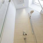 Shower with glass enclosure, showerhead, and handheld shower on floor tiles.