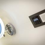 Wall-mounted control with display and speaker next to a lit mirror.