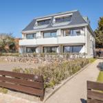 Modern multi-family house with balconies and stone wall. Access via walkway.