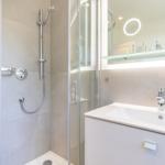 Shower with glass enclosure, sink and lit mirror