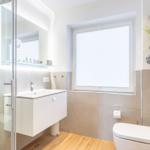 Bathroom with shower, sink and toilet. Wooden floor and window with blinds.