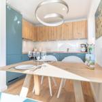 Dining area with wooden table and chairs. Kitchen with wooden cabinets and blue fronts.