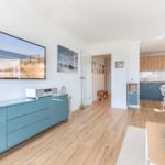 Living area with kitchen area, wooden floor, and sea view pictures on the wall.