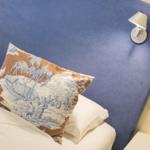 Bettkopfteil mit blauem Stoff, Kissen mit Landschaftsmotiv und Wandlampe.