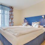 Schlafzimmer mit Doppelbett, blauem Kopfteil und Vorhängen mit Muster.