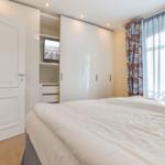 Schlafzimmer mit Doppelbett, Kleiderschrank und Fenster mit Vorhängen.