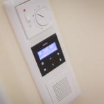 Wandmontierte Steuerung mit Temperaturregler und Digitaldisplay für Radio und Uhrzeit.