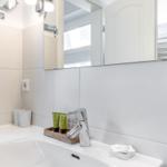 Badezimmer mit Waschbecken, Spiegel und Pflegeprodukten.
