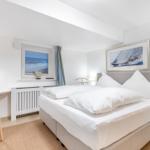 Schlafzimmer mit Bett, Schreibtisch und Meerblickfenster.