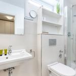 Badezimmer mit Dusche, Waschbecken und Spiegel. Drei grüne Flaschen auf dem Waschbecken.