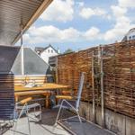 Terrasse mit Tisch, zwei Stühlen und Holz-Zaun. Hintergrund: Häuser und blauer Himmel.