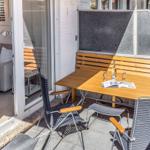 Terrasse mit Tisch, zwei Stühlen und Holzbank. Durchgang ins Wohnzimmer mit Sofa.