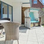 Terrace with dining table, chairs, and beach chair. Background: white plaster and wooden fence.