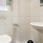 Bathroom with toilet, sink, and mirror on white tiled walls.