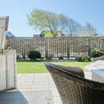Terrace with wicker chairs and table. Backyard with grass and wooden fence.