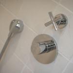 Shower head and controls mounted on tiled wall.