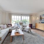 Living room with sofa, armchair, and coffee table. Windows overlook the garden.